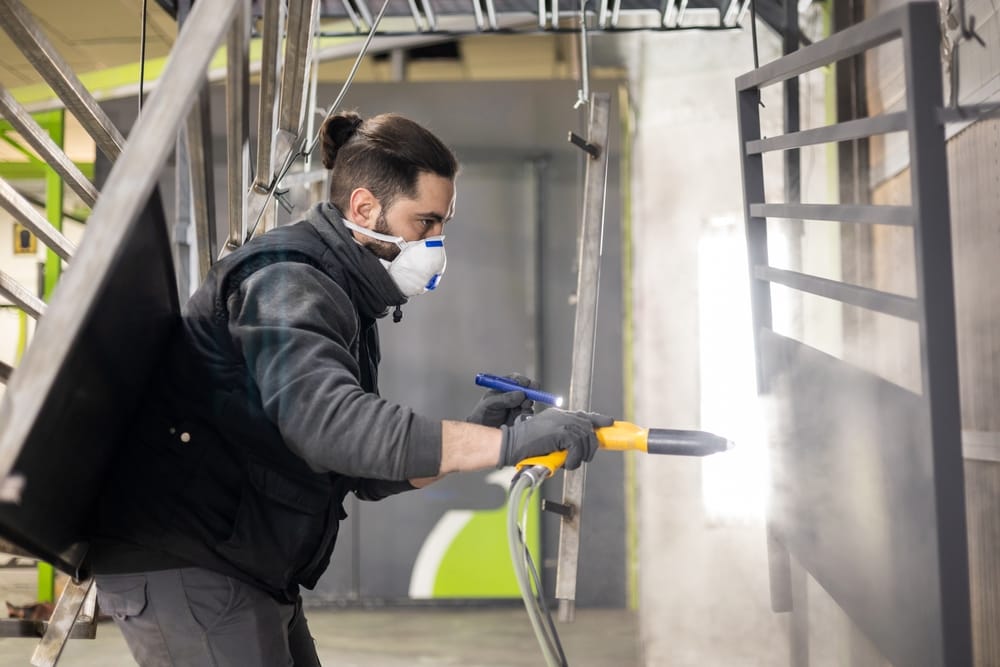 Un homme travaillant dans une usine termine un travail en utilisant la technique de revêtement par poudre électrostatique avec un pistolet pulvérisateur. Concept de travaux en usine métallurgique.